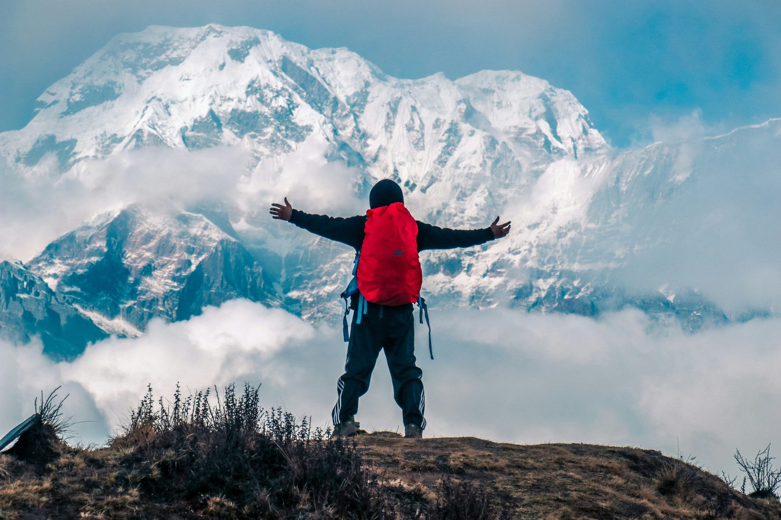 man raising both hands on mountain cliff with snow covered mountain view